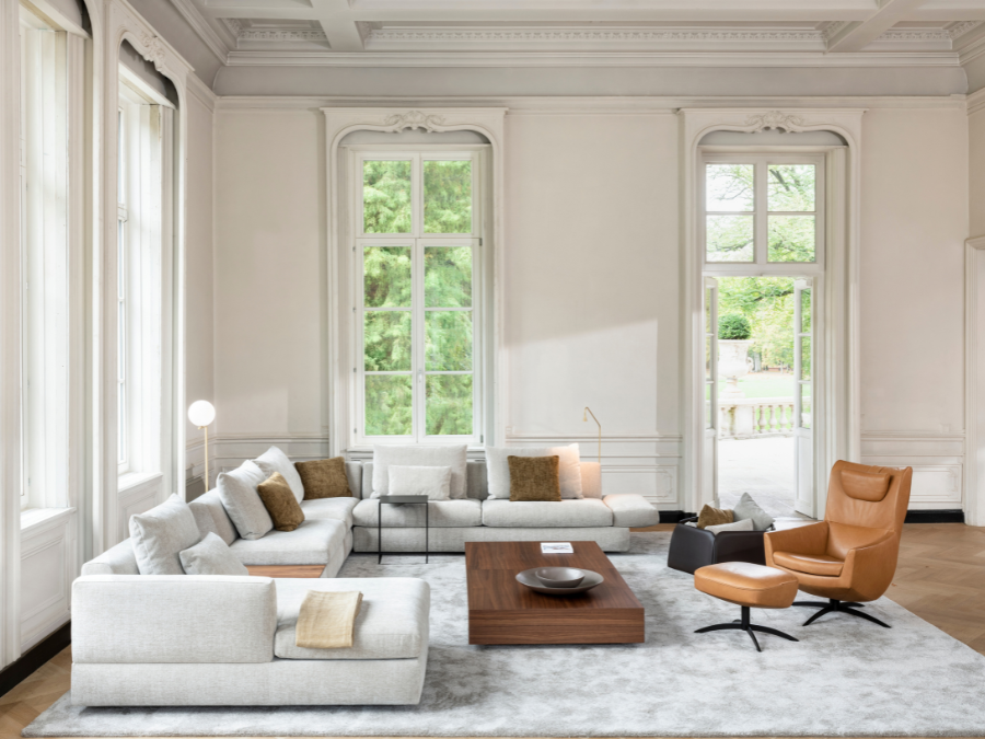 Lichtgrijze Jori Tigra Divanbase hoekzetel met longchair en okerkleurige kussens, notelaren salontafel en cognac lederen draaifauteuil met voetenbank in een klassiek salon