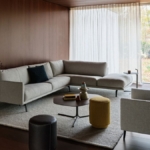 Leolux Bellice hoekbank in lichtgrijze stof met slanke metalen poten, met bijpassende fauteuil en poefs in een warme woonkamer met houten wanden