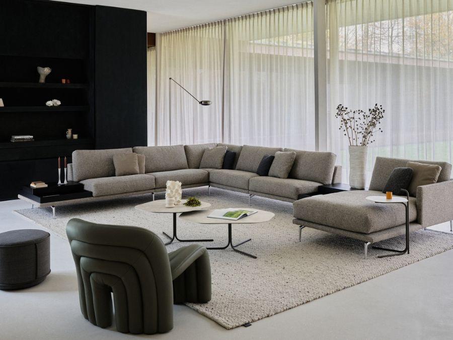 Grote Leolux Bellice hoekbank met longchair in grijze stof, met geïntegreerde bijzettafels en een groene lederen fauteuil in een lichte woonkamer
